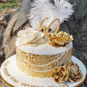 A white base adorned with white and golden roses, pearls and tall feathers.