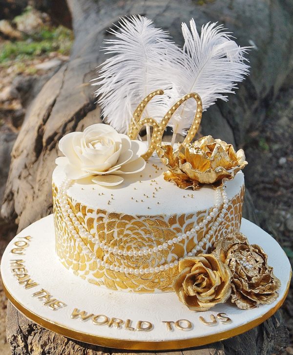 A white base adorned with white and golden roses, pearls and tall feathers.